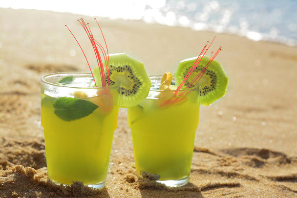 Glasses of refreshing drink with kiwi and mint on sand near sea - Фото, изображение