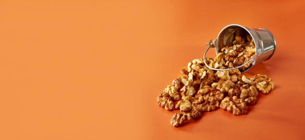 Een kleine metalen emmer gevuld met walnoten op een oranje achtergrond. Concept van gezond eten. - Foto, afbeelding