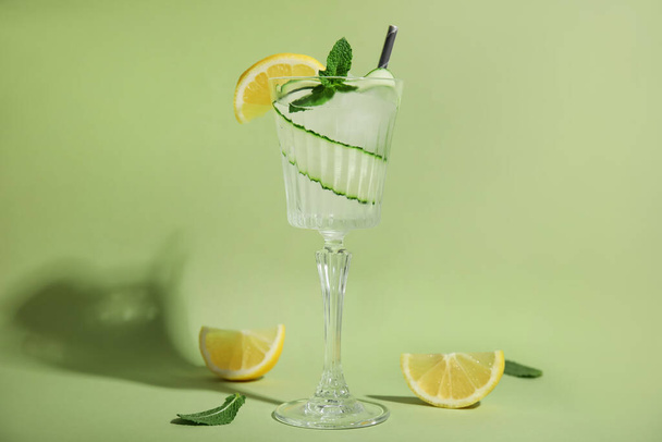 Glass of tasty fresh cucumber water with mint and sliced lemon on light green background - Fotó, kép
