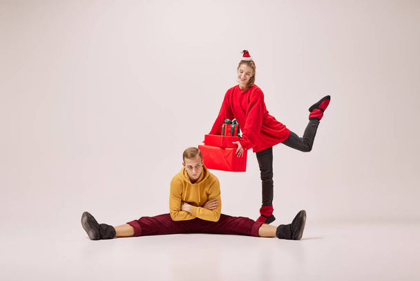 Dreams, love, happiness. Young and graceful couple of ballet dancers in warm winter clothes dancing with festive gift boxes on grey background. Christmas, New year, holidays, 2023, party concept - Fotó, kép