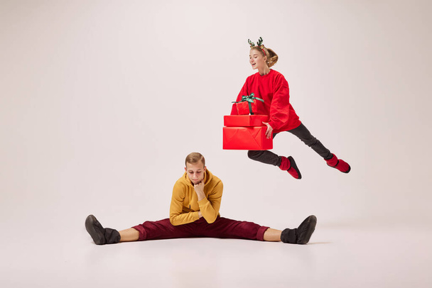 Christmas deer with presents. Flexible dancers, young happy couple in warm winter clothes dancing with festive gift boxes over grey background. Happy New year, holidays, 2023, party concept - Fotó, kép