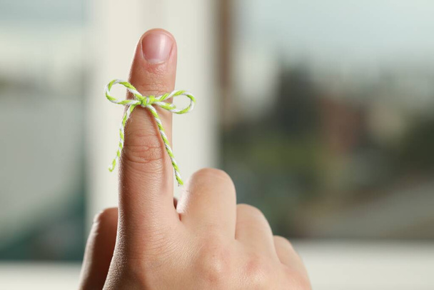 Man showing index finger with tied bow as reminder on blurred background, closeup - Foto, afbeelding
