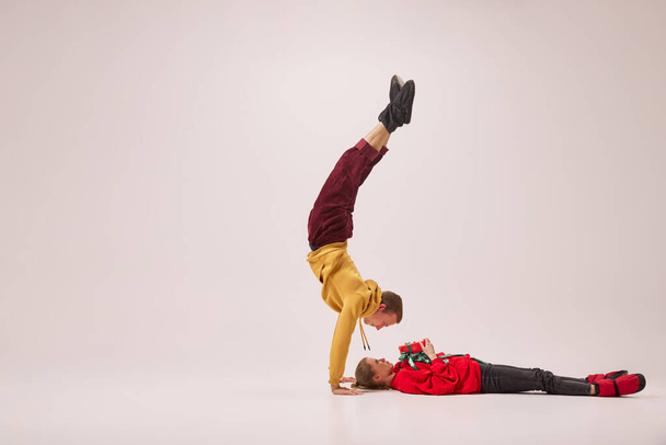 Fun, joy. Emotional flexible young couple of ballet dancers in warm winter homewear dancing isolated on grey background. Retro, vintage, dance, holidays, party concept. Copy space for ad - Foto, Bild