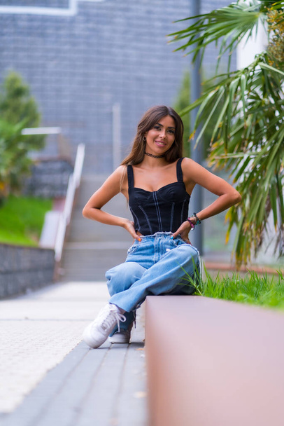 Portrait of a young brunette model in a black cap and jeans sitting in the city - Foto, Imagem