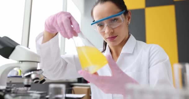 Le scientifique agite du liquide huileux jaune dans une fiole en laboratoire. Concept de recherche chimique - Séquence, vidéo