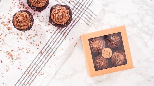 Flat lay. Step by step. Packaging chocolate cupcakes with chocolate ganache frosting into a paper cupcake box. - Photo, Image