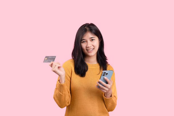 Портрет чудової жінки, що стоїть на жовтому тлі. тримає мобільний телефон, що показує пластикову кредитну картку
 - Фото, зображення