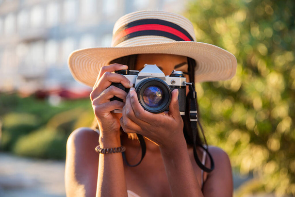 Νεαρή ελκυστική τουρίστρια παίρνει φωτογραφίες στην πόλη με αναλογική φωτογραφική μηχανή της. - Φωτογραφία, εικόνα