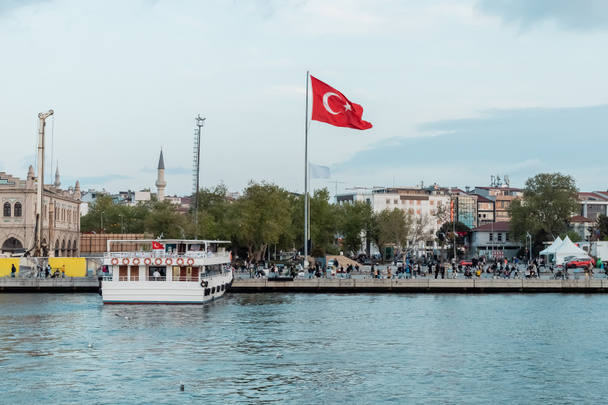 ISTANBUL, TURKEY - MAY 8, 2022: red turkish flag near seashore and boat on pier near bosporus in istanbul  - Photo, image