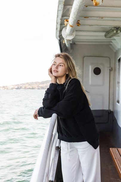 jovem sonhadora em camisola preta olhando para o mar de barco de balsa cruzando bosporus em istanbul  - Foto, Imagem