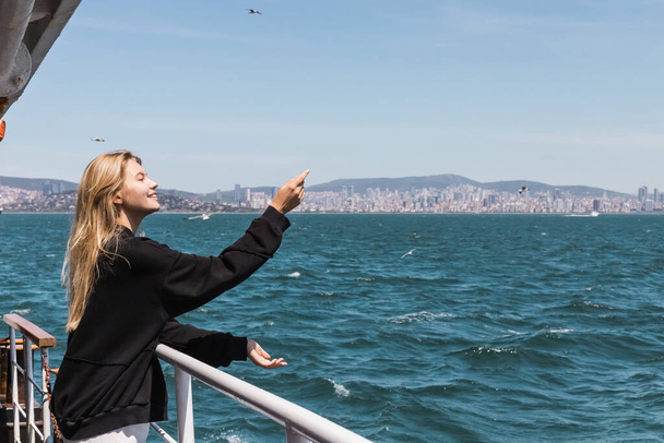 happy woman in black sweater gesturing and looking at sea from ferry boat crossing bosphorus strait - Photo, Image