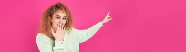 A young girl with curly hair points with a gesture on a studio background. - Photo, image