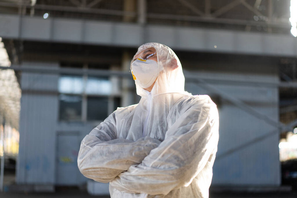 COVID-19 coronavirus doctor standing hospital parking dressed white protective overalls hazmat suit. Infectious disease pandemic medical worker front line, outbreak. Male medical worker medium shoot - 写真・画像