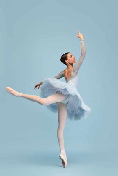 Portrait of tender young ballerina dancing, performing isolated over blue studio background. Standing on tiptoe. Concept of classic ballet, inspiration, beauty, dance, creativity - Photo, Image