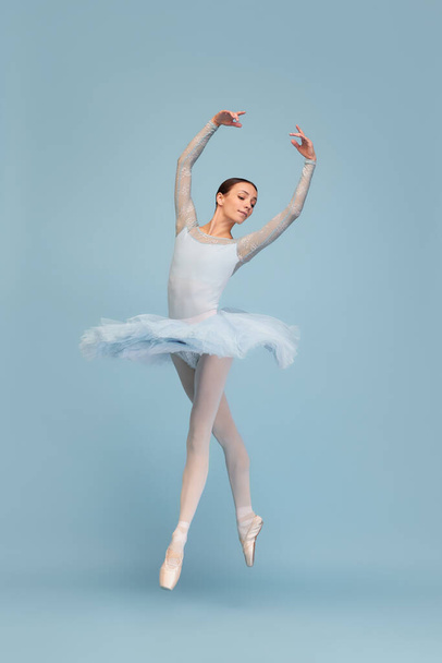 Retrato de la tierna bailarina joven bailando, actuando aislada sobre fondo de estudio azul. Belleza de la coreografía. Concepto de ballet clásico, inspiración, belleza, danza, creatividad - Foto, imagen