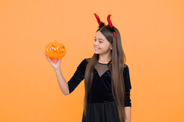look what i have. cheerful kid hold creepy pumpkin. carnival costume party. trick or treat. celebrate the holidays. jack o lantern. halloween devil girl. happy childhood. teenage child in imp horns. - Fotografie, Obrázek