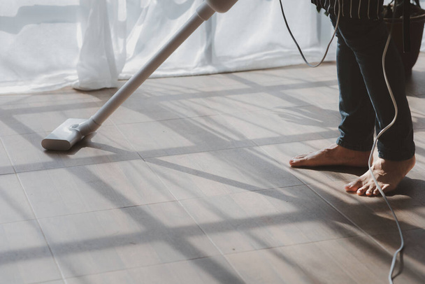 Person cleaning room, cleaning worker is using a vacuum cleaner to clean the living room floor in the company office. Cleaning staff. Maintaining cleanliness in the organization. - 写真・画像