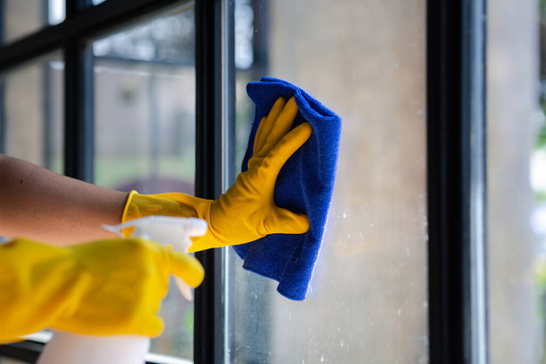 La persona che pulisce la stanza, il personale di pulizia utilizza un panno e spruzza disinfettante per pulire il vetro nella stanza dell'ufficio aziendale. Personale di pulizia. Mantenere la pulizia nell'organizzazione. - Foto, immagini