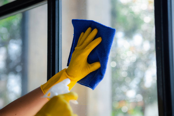 Osoba sprzątająca pokój, personel sprzątający używa tkaniny i środka dezynfekującego do wycierania szkła w biurze firmy. Sprzątacze. Utrzymanie czystości w organizacji. - Zdjęcie, obraz