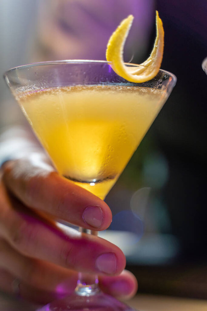 Close-up of a barmans hand serving a beautiful yellow cocktail on the bar counter in the nightclub. High quality photo - Foto, Bild