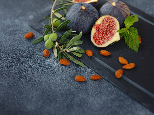 fresh ripe figs fruit almond nuts and olive branch on dark table. mediterranean food concept - Photo, image