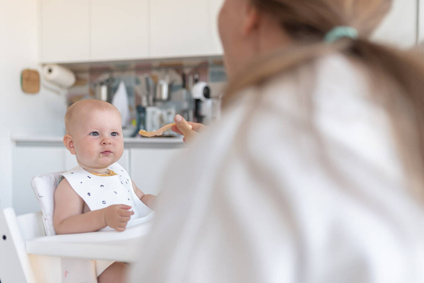 babys first feeding, mom feeds a surprised baby with a spoon. High quality photo - Foto, afbeelding