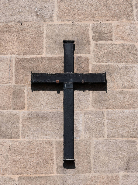 Black colored metal christian cross casting its dark shadow on a stone brick facade of a church - Photo, Image