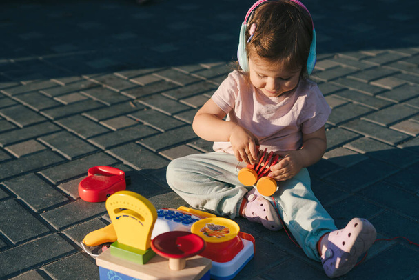 Glimlachend klein meisje dat buiten speelt met kleurrijk plastic speelgoed in de tuin. Baby ontwikkeling. Kinderopvang. - Foto, afbeelding