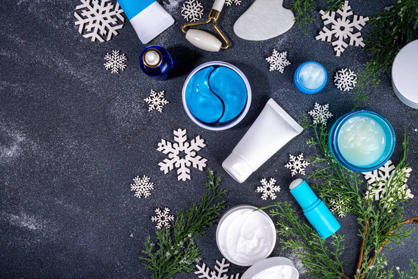 Winter skin care and hand care cosmetic in unbranded containers, bottles, tubes with artificial snowflakes on black stone background. Winter hand skin care cosmetics background top view copy space - Foto, Imagen