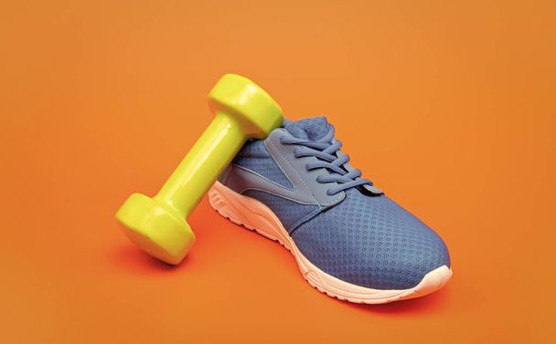 comfortable blue sport shoe with barbell on orange background, sport accessory. - Foto, imagen