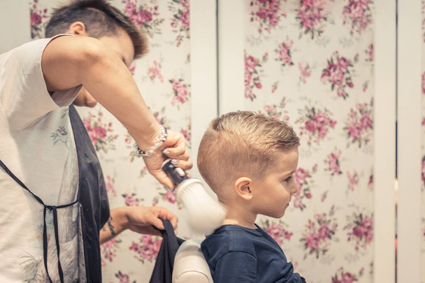Hairdresser cleaning boys neck with barber brush after the haircut at  salon. - Fotó, kép