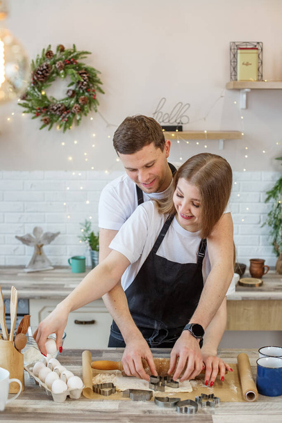 若い幸せなカップルは彼らの台所で一緒にクリスマスクッキーを楽しみ、準備する。家族、クリスマス休暇、趣味のコンセプト. - 写真・画像