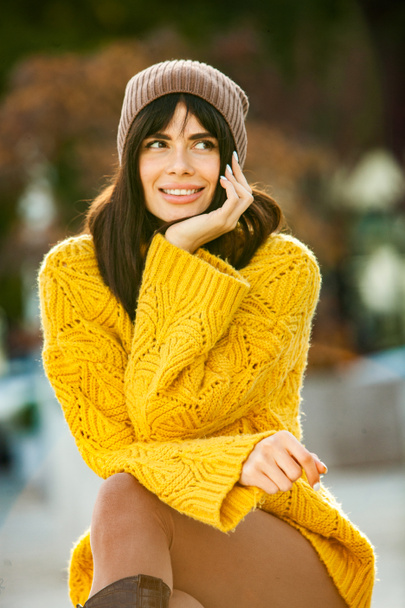 美しいヨーロッパのブルネットは黄色のウールのセーターと帽子を外で着ていました。涼しい天気の中で太いスタイリッシュな秋の服を身に着けている美しい女の子. - 写真・画像
