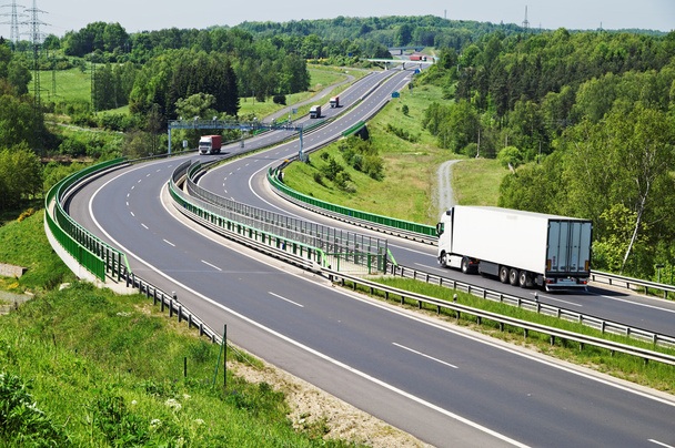 die Autobahn zwischen Wäldern, in der Mitte der Autobahn elektronische Mautstellen, fahrende Lastwagen - Foto, Bild