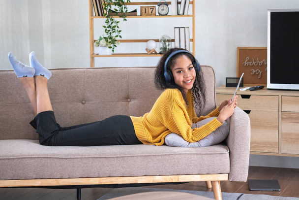 An African American woman uses a laptop, smartphone, tablet and music headset in her home to relax. - Zdjęcie, obraz