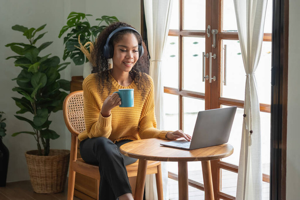 アフリカ系アメリカ人の女性がリラックスするために自宅でノートパソコン、スマートフォン、タブレット、音楽ヘッドセットを使用しています. - 写真・画像