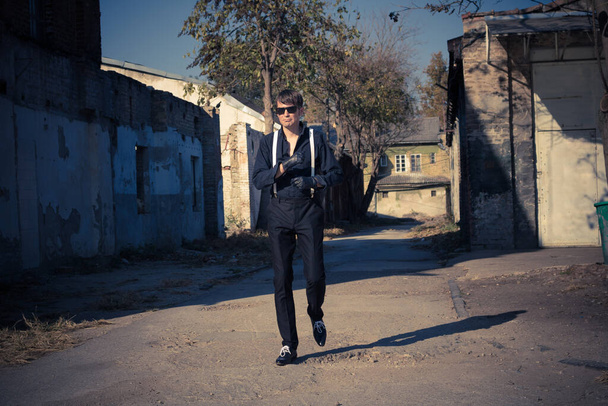 Full length of serious man in black outfit walking outdoors. - 写真・画像