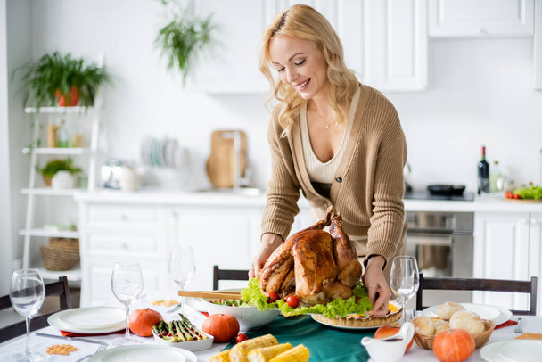 Smiling woman putting thanksgiving turkey on table at home  - Фото, зображення
