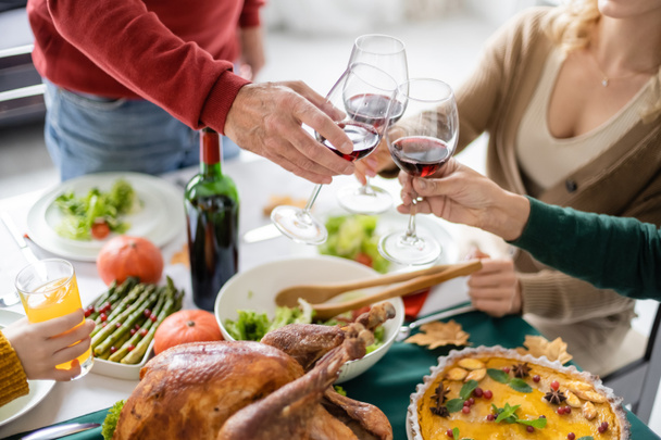 Vista ritagliata di famiglia brindare con vino vicino deliziosa cena del Ringraziamento a casa  - Foto, immagini