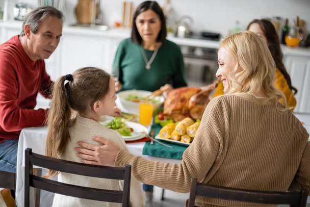 Smiling mother hugging kid near blurred multiethnic family celebrating thanksgiving at home - 写真・画像