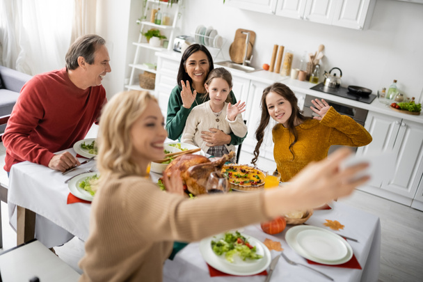 Iloinen rotujenvälinen perhe heiluttaa käsiään selfien ja kiitospäivän illallisen aikana kotona - Valokuva, kuva