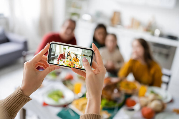 Woman taking photo of multiethnic family near thanksgiving dinner at home  - Zdjęcie, obraz
