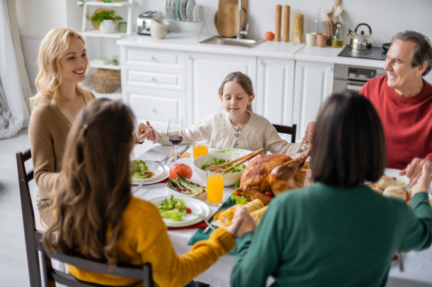 Smiling family holding hands near thanksgiving dinner with drinks at home  - Photo, Image