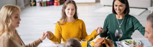多文化家族が自宅でテーブルの上でおいしい感謝祭ディナーの近くに手を握る、バナー  - 写真・画像