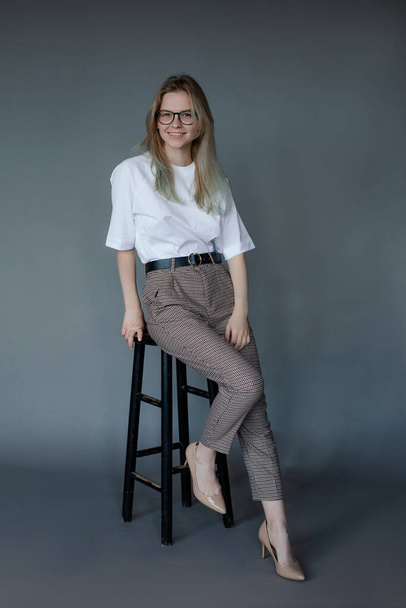 Full length photo of joyful beautiful woman in office style outfit sit on chair, gray background, free copy space. New collection of casual clothes for business people. Working lifestyle concept. - 写真・画像
