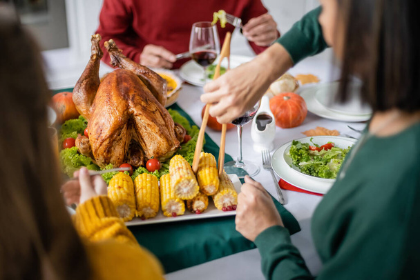 Woman taking corn during thanksgiving dinner with family at home  - 写真・画像