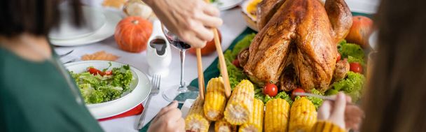 Cropped view of woman taking corn near grandchild and thanksgiving turkey at home, banner  - Foto, imagen