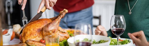 Cropped view of senior man cutting delicious thanksgiving turkey near dinner at home, banner  - Foto, imagen