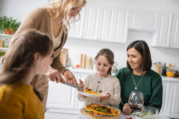Woman putting thanksgiving pie on plate near interracial family at home  - Фото, изображение