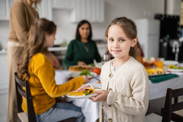 Child holding thanksgiving pie near blurred family at home  - Photo, Image